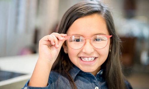 Little girl trying glasses at the optician - healthcare and medicine concepts
